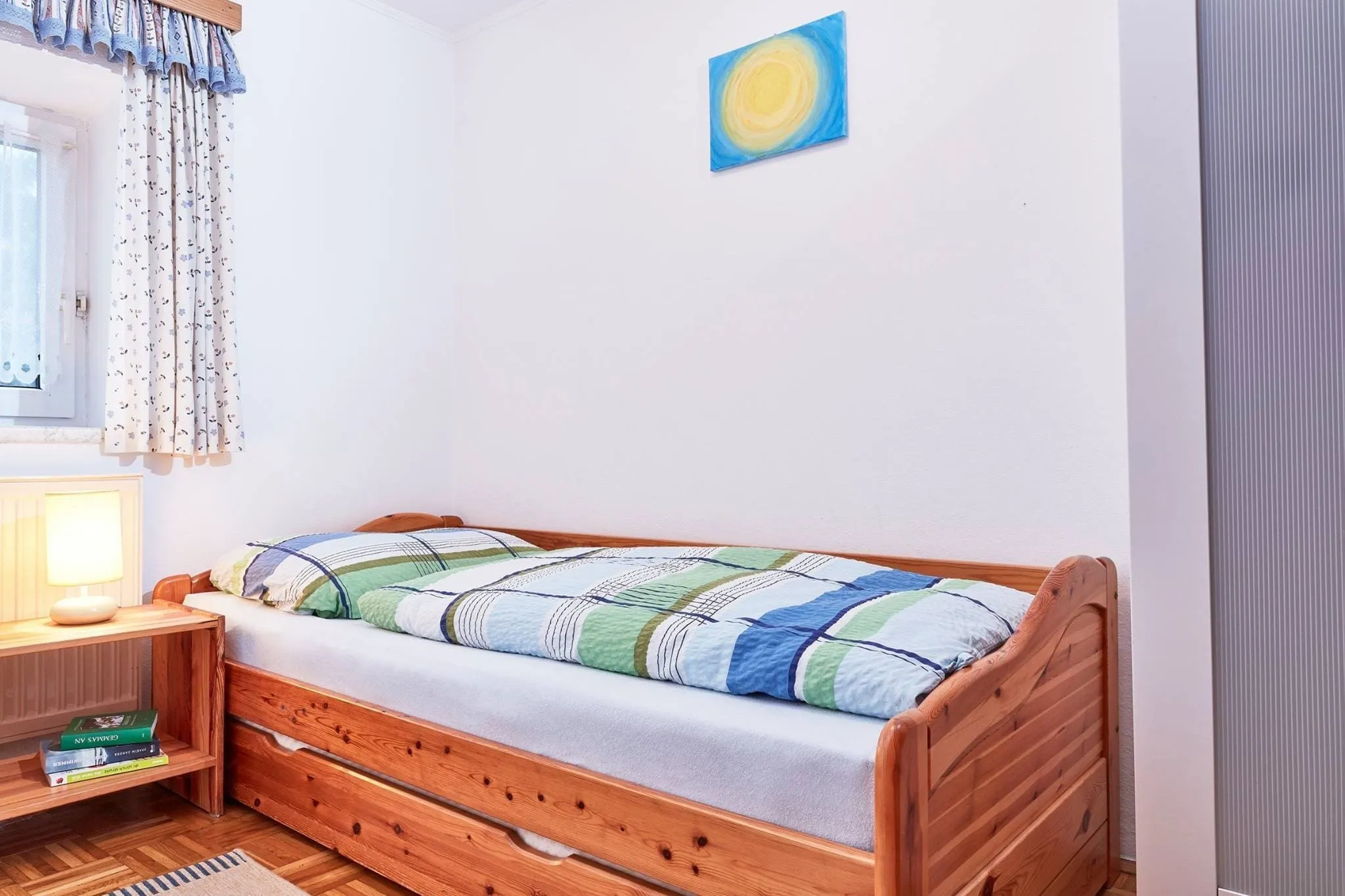 Kleines Schlafzimmer der Ferienwohnung Zwei mit Einzelbett aus Holz und Nachtkästchen